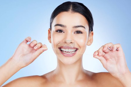 Téléchargez les photos : Face, flossing teeth and hygiene with woman, dental and beauty with grooming and mouth care on blue background. Hands, string and healthy gums with fresh breath, health and skin glow in portrait. - en image libre de droit