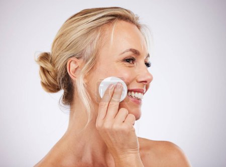 Foto de Face, cotton and skincare with a mature woman in studio on a gray background cleaning her skin for exfoliation. Relax, luxury and product with a female using a pad to cleanse her pores for beauty. - Imagen libre de derechos