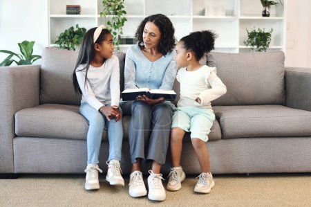 Photo for Senior family reading books to children, teaching and learning bible story, questions and education in living room. Grandmother and kids on sofa with storytelling or holy religion, knowledge and help. - Royalty Free Image