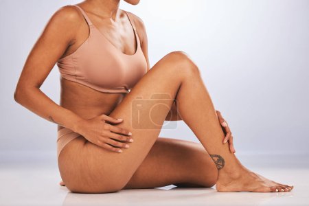 Photo for Hands, legs and skincare with a black woman in studio, sitting on the floor against a gray background for beauty. Fitness, body and tattoo with a female posing for hair removel, wax or laser. - Royalty Free Image
