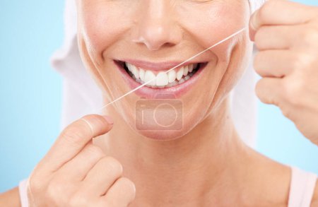 Téléchargez les photos : Floss, dental wellness and mouth of woman in studio for beauty, healthy face and happiness on blue background. Closeup model, tooth flossing and cleaning for facial smile, mint breath and happy teeth. - en image libre de droit