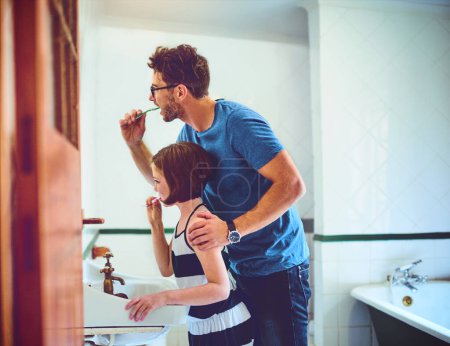Getting through their daily routine together. a father and his little daughter brushing their teeth together at home