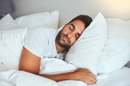 Téléchargez les photos : Un peu de repos après une dure journée de travail. un beau jeune homme dormant confortablement dans son lit à la maison - en image libre de droit