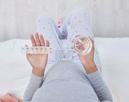 Téléchargez les photos : Pregnant, medicine and water in woman hands above pills box for health, growth and wellness. Person in home bedroom with a glass and Pharma product container for pregnancy supplement and development. - en image libre de droit