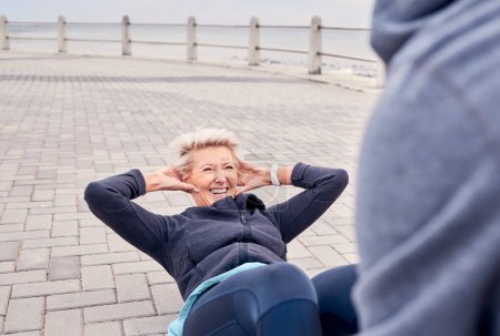 Photo for Senior woman, fitness and sit ups with personal trainer at the beach for strong ab workout or exercise. Happy elderly female smile for core, stomach or abdomen training with health coach by the sea. - Royalty Free Image
