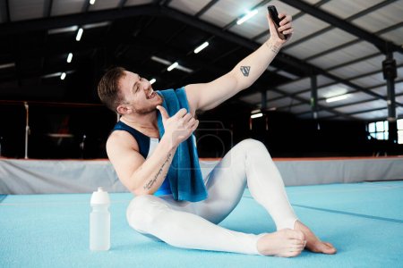 Photo for Man, gymnast and thumbs up for fitness selfie, profile picture or vlog in social media sitting on floor at the gym. Happy male acrobat smile for photo, memory or post showing thumb emoji, like or yes. - Royalty Free Image