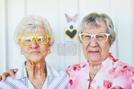 Téléchargez les photos : Faire des années dorées des années funky. Portrait de deux femmes âgées heureuses portant des lunettes funky à la maison - en image libre de droit