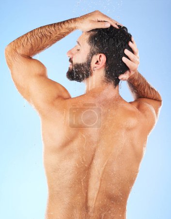 Foto de Water, shower and back of man in studio for skincare, wellness and shampoo cosmetics on blue background. Hair, body and male model cleaning with water, beauty and dermatology on bathroom backdrop. - Imagen libre de derechos