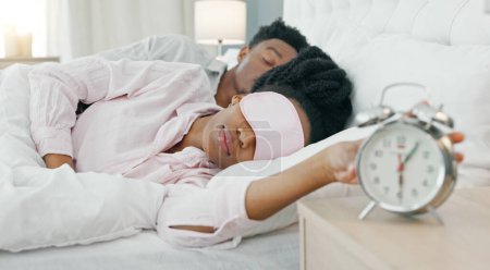 Téléchargez les photos : Femme noire se réveillant au lit pour éteindre son réveil avec un masque de sommeil dans sa maison. Fille paresseuse, somnolente et africaine dormant dans sa chambre confortable avec un lever tôt le matin heure à la maison - en image libre de droit