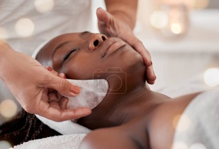 Téléchargez les photos : Femme noire, massage gua sha et traitement du visage de luxe d'une jeune femme avec spa facial. Soins de la peau, outil en quartz rose et beauté dans une clinique de bien-être avec le client se sentant calme et zen de la dermatologie. - en image libre de droit