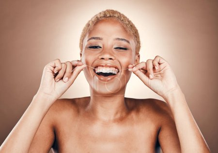 Téléchargez les photos : Black woman, flossing teeth and dental care portrait on a brown background for healthy smile. Laughing model person in studio for self care, cleaning mouth and funny hygiene for health and wellness. - en image libre de droit