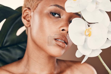 Téléchargez les photos : Flower, portrait and black woman with cosmetics, dermatology and treatment for wellness and confidence. Face, female and lady with plant, orchid and natural care for luxury, healthy and smooth skin. - en image libre de droit