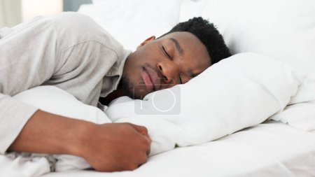 Foto de Dormir, relajarse y soñar con un hombre negro en casa en la cama en una mañana de fin de semana. Cansado, durmiendo y soñando solo en el dormitorio. Relajante, la paz y la comodidad con la cabeza en la almohada para el tiempo de sueño en la habitación luminosa - Imagen libre de derechos