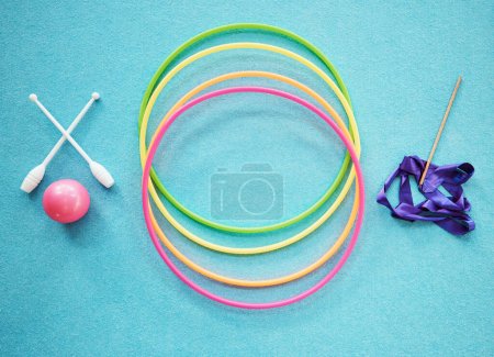 Gymnastics, dance and fitness with a hula hoop, ribbon and bars on an empty blue floor from above for exercise or training. Exercise, workout and still life with equipment for dancing or performance.