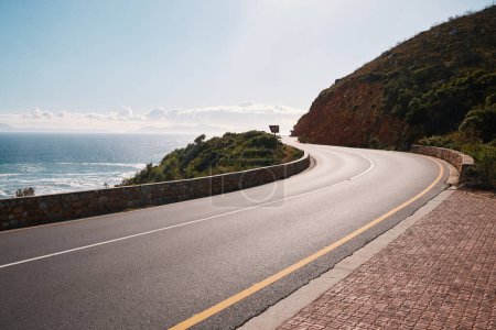 Photo for Mountain, road and ocean view with no people for travel, destination or sightseeing in Cape Town. Nature, beauty on empty street for road trip, vacation or holiday on South Africa blue sky background. - Royalty Free Image