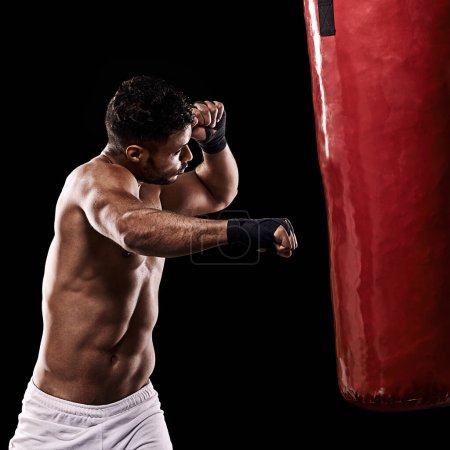 Photo for Delivering a powerful right hook. Studio shot of kick boxer working out with a punching bag against a black background - Royalty Free Image