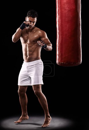 Photo for Have you had enough. Studio shot of kick boxer working out with a punching bag against a black background - Royalty Free Image