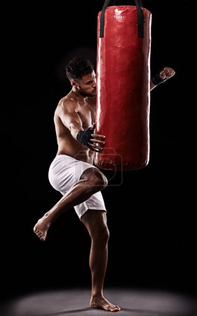 Beim Kampfsport geht es nicht darum, seinen Baucharakter zu bekämpfen. Studioaufnahme eines Kickboxers, der mit einem Boxsack vor schwarzem Hintergrund trainiert