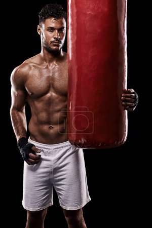 Photo for Train hard and be the best. Studio shot of kick boxer working out with a punching bag against a black background - Royalty Free Image