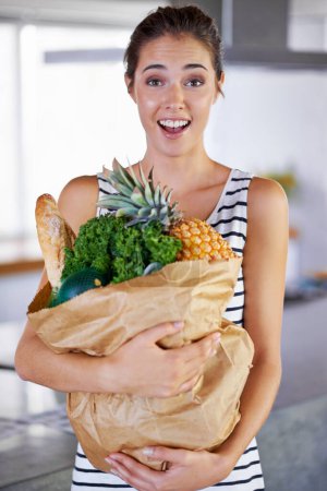 Good food, great attitude. An attractive woman holding a bag of groceries in the kitchen Poster 645281312