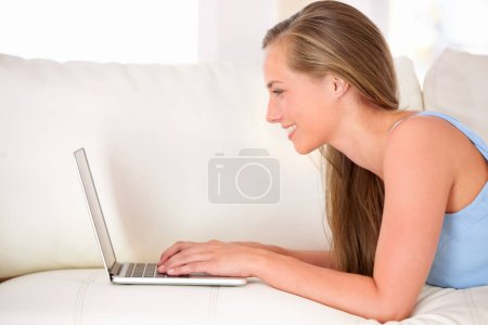 Chatting with friends online. an attractive young woman using a laptop while lying on the sofa Poster 645282558
