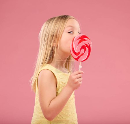 Photo for Candy, sweets and lollipop with girl in studio for sugar, party and carnival food isolated on pink background. Cute, positive and youth with child and eating colorful snack for playful and treats. - Royalty Free Image