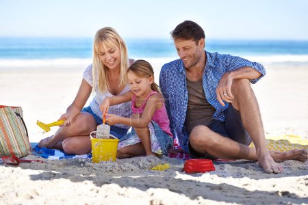 Téléchargez les photos : Faire un château de sable. une jeune famille heureuse qui s'amuse à la plage - en image libre de droit