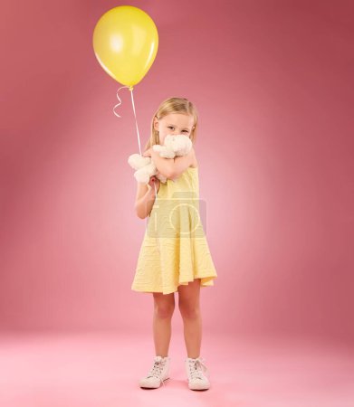 Teddy bear kiss, balloon and girl portrait with a soft toy with happiness and love for toys in a studio. Isolated, pink background and a young female child feeling happy, joy and cheerful with friend.