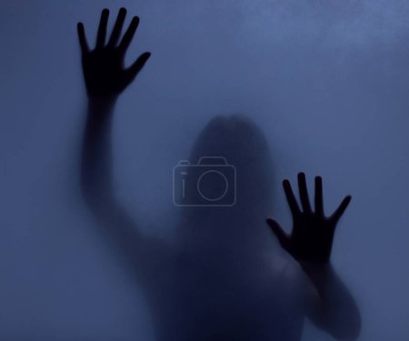 Horror, mystery and shadow of a woman on a window for fear, escape or nightmare. Dark, hands and a ghost, girl or person with paranormal activity, spooky behavior or strange movement in a studio.