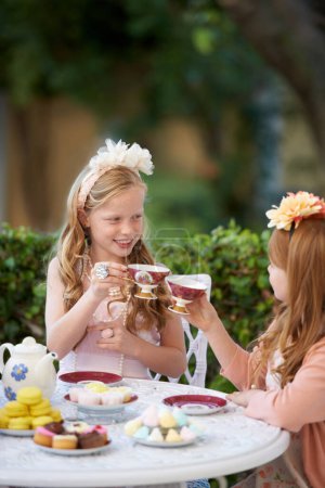 Téléchargez les photos : Faire un goûter imaginaire. Deux jeunes filles faisant une partie de thé dans le jardin - en image libre de droit