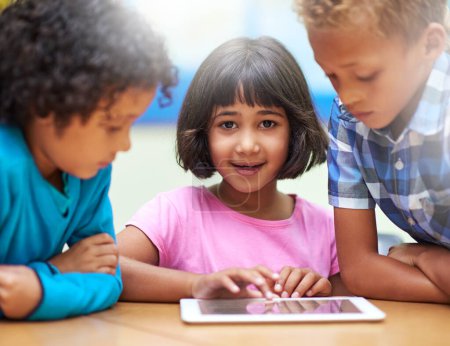 Foto de Conectado en el aula. niños de primaria que usan una tableta digital mientras están sentados en clase - Imagen libre de derechos