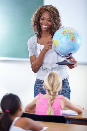 Photo for Who can tell me the name of this country. A young teacher showing her class a globe of the world during geography - Royalty Free Image