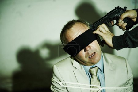 Foto de Si nuestras demandas no se cumplen, está muerto. Un hombre de negocios con los ojos vendados con un arma en la cabeza junto al espacio de copia - Imagen libre de derechos