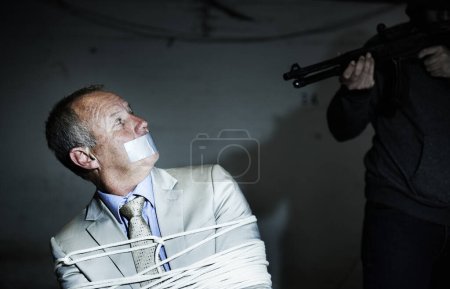 Photo for Staring down the barrel of a gun. A bound and gagged businessman staring at the barrel of his assailants rifle - Royalty Free Image