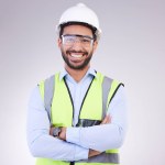 Construction worker in portrait, man with crossed arms and smile, architect or engineer in building industry on studio background. Happy contractor, professional builder with helmet and goggles.