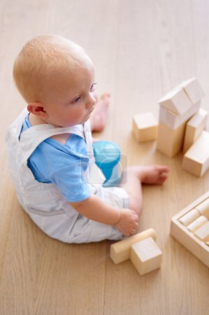 Hes a future architect. A little boy sitting on the ground with his wooden blocks