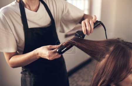 Photo for Hair doesnt make the woman, but good hair definitely helps. a hairstylist using a curling iron to do her clients hair - Royalty Free Image