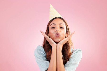 Birthday woman, face portrait and kiss for celebration event, congratulations or celebrate studio happiness. Emoji gesture, party hat and headshot female, person or young model on pink background.