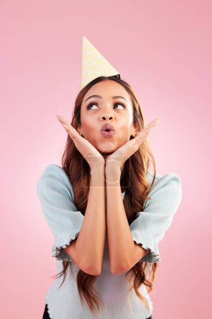 Birthday woman, studio and blowing kiss for celebration event, congratulations or celebrate happiness. Emoji gesture, party hat and relax female, person or young model looking on pink background.