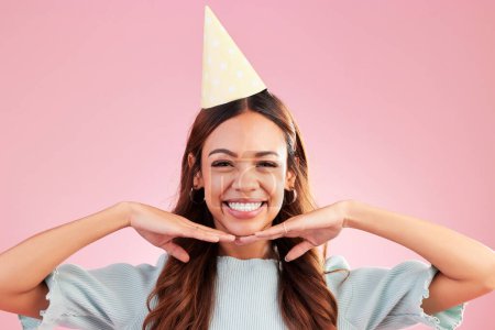 Birthday woman, face portrait and smile for happy celebration event, congratulations or celebrate happiness. Studio posing, party hat and headshot female, person or young model on pink background.
