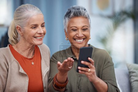 Foto de Las mujeres mayores sonríen, llaman a las redes sociales y a la sala de estar con mujeres mayores en el móvil web. Transmisión de vídeo, felicidad y conversación en una casa con personas mayores juntas sobre tecnología en el hogar. - Imagen libre de derechos
