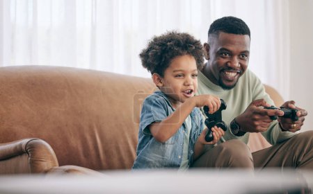 Schwarze Familie, Vater und Kind spielen Videospiele auf dem Wohnzimmersofa zusammen mit Controllern zu Hause. Glücklicher afroamerikanischer Vater mit Sohn mit Lächeln genießt Bondzeit auf Konsolenunterhaltung.