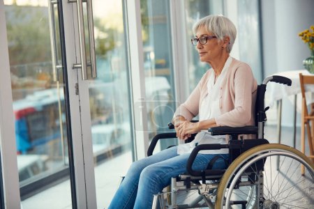 Foto de Si yo fuera más fuerte, hubiera estado fuera. una mujer mayor mirando reflexivo mientras está sentada en su silla de ruedas en una casa de retiro - Imagen libre de derechos