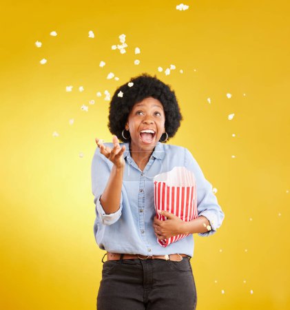 Photo for Happy, throwing and popcorn with black woman in studio for movie, streaming service and cinema. Laugh, funny and theatre with female and snack isolated on yellow background for food, tv and film. - Royalty Free Image