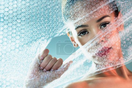 Photo for Bubble wrap, beauty and portrait of woman with makeup, cosmetics and skincare products in studio. Creative art, salon aesthetic and girl with face glow, lipstick and luxury style with plastic tear. - Royalty Free Image
