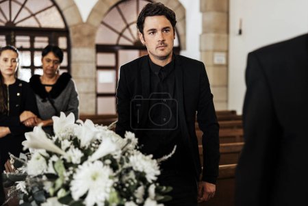 Funeral, death and grief with a man pallbearer carrying a coffin in a church during a ceremony. Flowers, suit and loss with a male holding a casket while walking through a chapel for mourning.