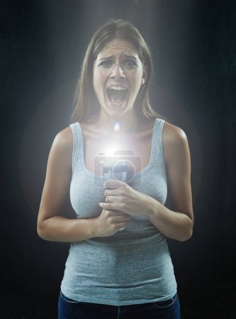 Photo for Horror movies have made her paranoid about the dark. A young brunette holding a flashlight while looking scared and isolated on a black background - Royalty Free Image