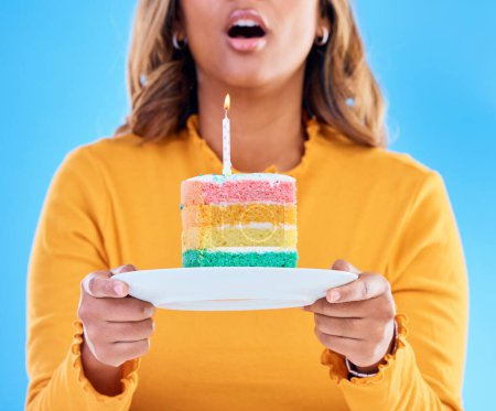 Birthday cake, celebration and blowing a candle to celebrate a gift or present isolated in a studio blue background. Dessert, sweet and woman or person excited, happiness and happy for festive.