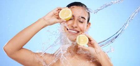 Beauty, lemon and water splash with woman in studio for natural cosmetics, nutrition and detox. Glow, fruits and hydration with female on blue background for diet, clean face and vitamin c skincare.