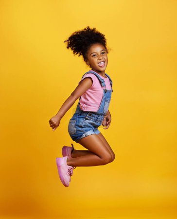 Excited, jump and happy girl child jumping in happiness, joy and smile while isolated in a studio yellow background. Energy, celebrate and kid in the air due to winning, celebrating and succuss.